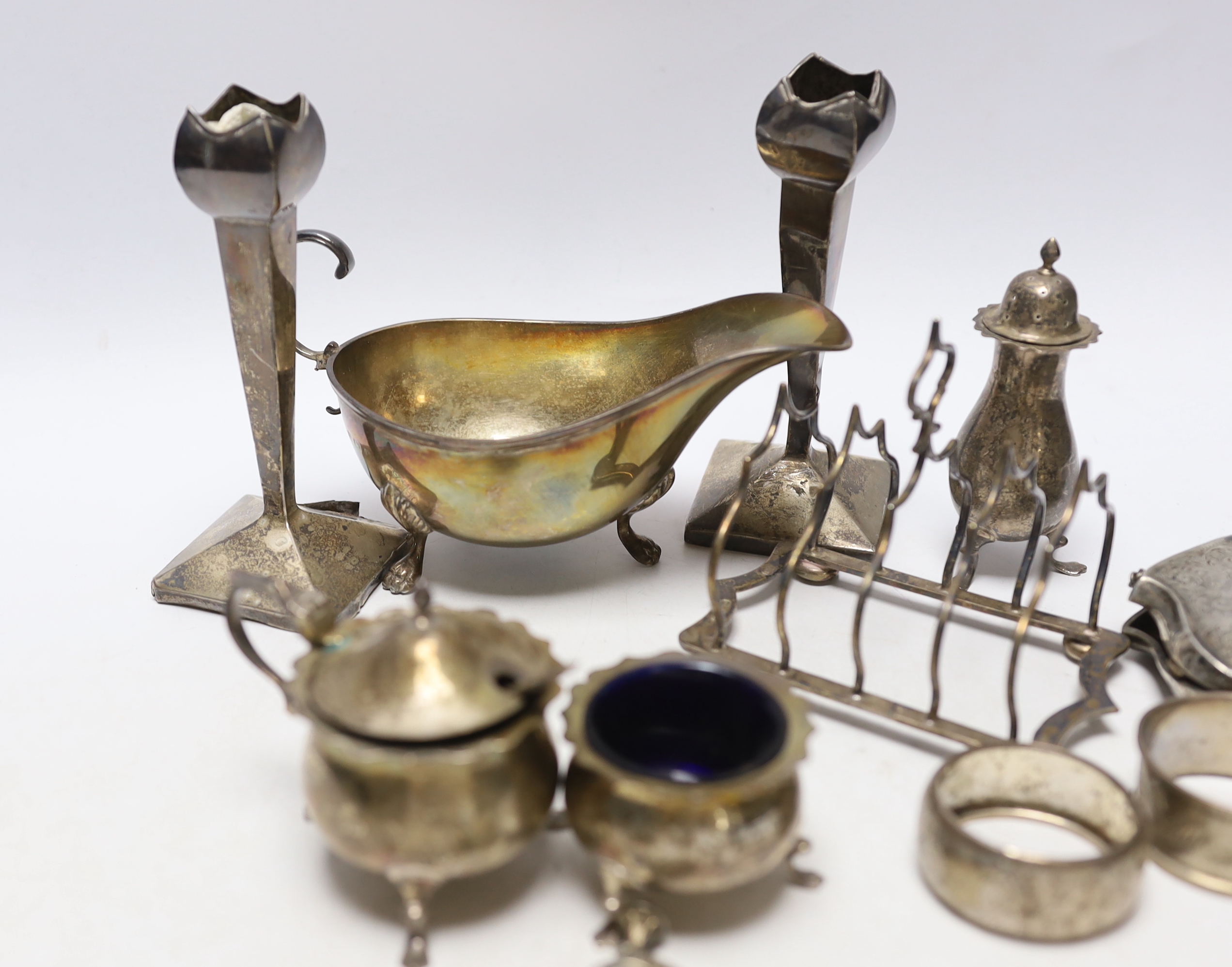 Sundry small silver including an Edwardian silver sauceboat, Birmingham, 1906, pair of spill vases (a.f.), a five bar toastrack, three condiments, a purse, two napkin rings and a child's rattle.